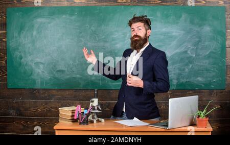 Teacher bearded man tell interesting story. Teacher charismatic hipster stand near table classroom chalkboard background. Teacher interesting interlocutor best friend. Talking to students or pupils. Stock Photo