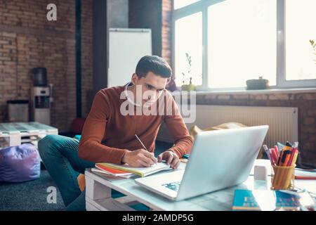 Dark-haired student making notes while watching educational video Stock Photo