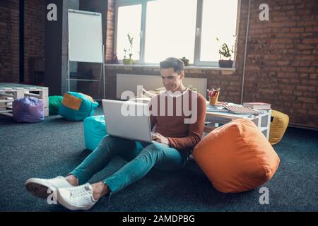 Dark-haired freelancer sitting on the floor with laptop while working Stock Photo