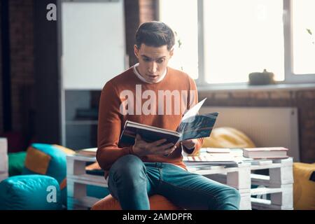 Dark-haired student feeling surprised while reading book Stock Photo