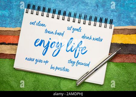 enjoy life - healthy, happy and positive lifestyle word cloud on a sketchbook against colorful paper abstract landscape Stock Photo