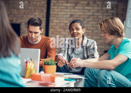 Dark-skinned student feeling thoughtful while studying with friends Stock Photo