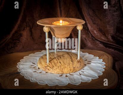 Multi-part wooden candlestick with burning candle stands on a dark wooden board against brown background Stock Photo