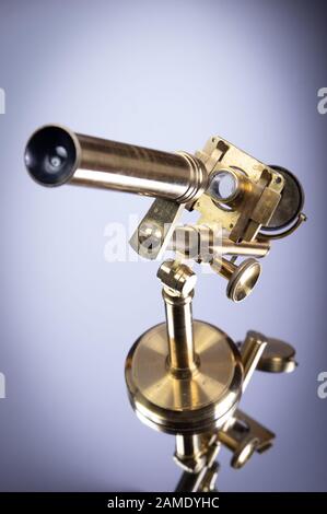 Old brass microscope standing on mirror Stock Photo