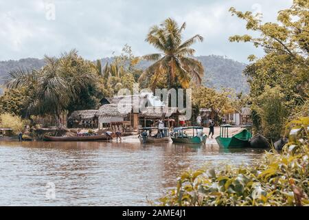 MAROANTSETRA, MADAGASCAR OCTOBER 19.2016: Small village harbor on the Antainambalana River, boats are moored in the harbor and local women wash dishes Stock Photo