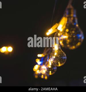 Retro style incandescent light bulb garland as decoration of a city street at night. Lamps on a black background. Stock Photo