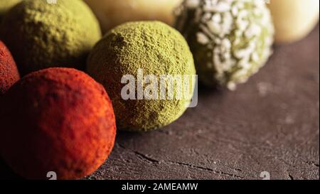 Colorful homemade truffles coated in dry beet powder, matcha tea powder, shredded cococnut on dark background. Copy space for text or design, banner. Stock Photo