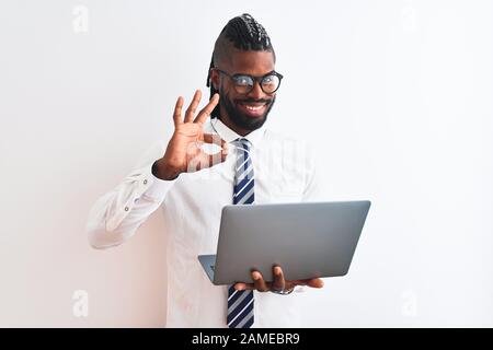 African american businessman with braids using laptop over isolated white background doing ok sign with fingers, excellent symbol Stock Photo