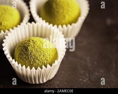 Homemade truffles candy with matcha tea powder in white paper cups on dark background. Copy space right for text or design. Shallow depth of field Stock Photo