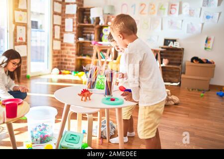 Beautiful teacher and toddlers playing cooking with plastic food around lots of toys at kindergarten Stock Photo