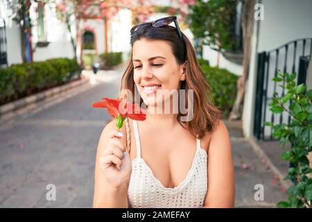 Young beautiful woman at the colorful village of Puerto de Mogan, smiling happy smelling flower on the street on summer holidays Stock Photo