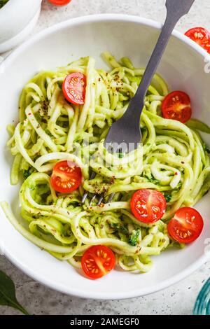 Zucchini pasta with pesto, avocado and tomatoes in a white plate. Raw vegan food concept. Stock Photo