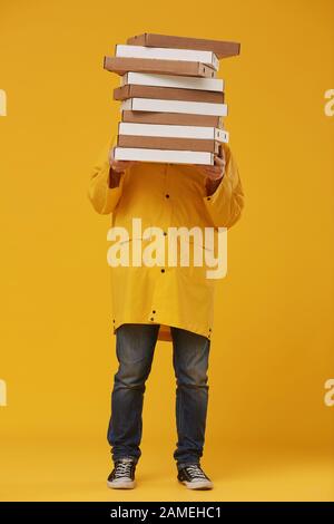 Full length portrait of unrecognizable delivery man hiding behind pizza boxes while standing against pop yellow background in studio Stock Photo