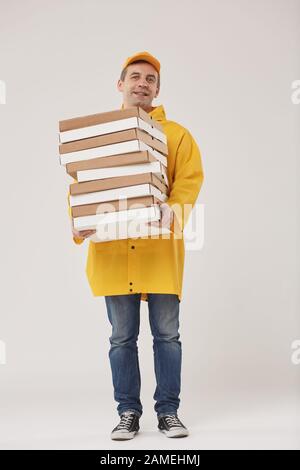 Full length portrait of adult delivery man holding pizza boxes and smiling cheerfully at camera while standing against white background Stock Photo