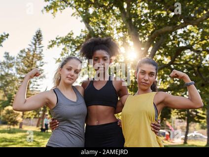 Sporty healthy young multiethnic female friends flexing their muscle looking at camera in the park - strong woman depicting female power  Stock Photo