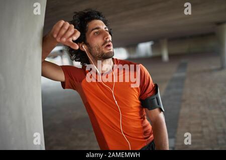 Portrait of a fitness athlete man in earphone breathing heavily after running and doing exercise - exhausted athlete runner Stock Photo