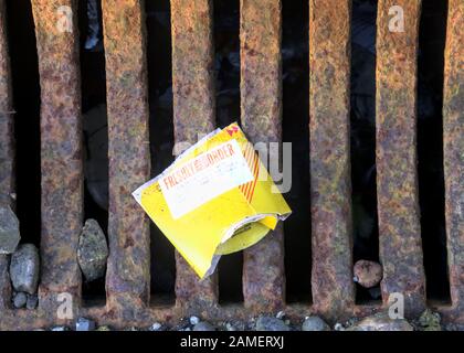 Yellow McDonalds food wrapper litter in the street laying on top of a street drain grate. Stock Photo