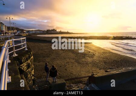 Couple stand on the breakwater looking at the setting sun in the university town of Aberystwyth Wales UK Stock Photo