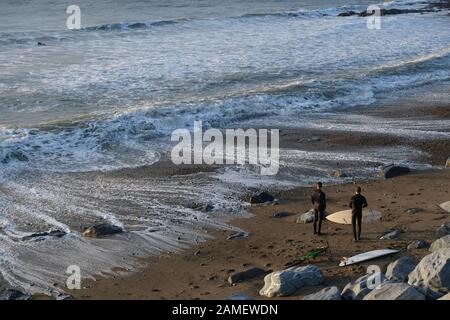 Aberystwyth Ceredigion UK January 10 2019: Two surfers with surfboards on the beach preparing to join their friend already in the sea Stock Photo
