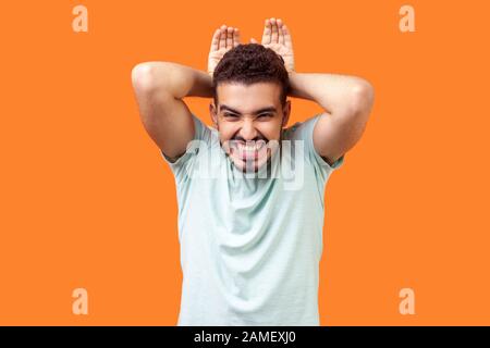 Portrait of funny joyous brunette man with beard in casual white t-shirt showing bunny ears gesture, looking hilarious and excited, fooling around. in Stock Photo