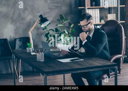 Profile photo of handsome business guy reading paper report holding hand on chin thoughtful important documents wear specs black blazer shirt suit Stock Photo
