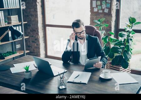 Photo of attentive handsome business guy focused on reading e-reader report checking finance information wear specs black blazer shirt suit sitting Stock Photo
