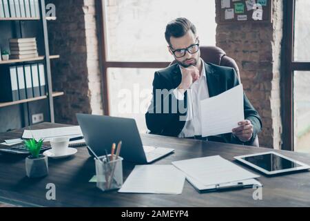 Photo of handsome business brunet guy reading paper report noticed wrong income stats numbers looking for mistakes wear black blazer shirt suit Stock Photo