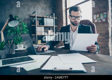 Photo of attentive handsome business brunet guy notebook table reading paper report before filling online statistics wear black blazer white shirt Stock Photo