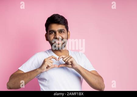 I love you. Happy cheerful unshaven man showing heart gesture over chest, cute smiling, expressing his love and affection to girlfriend, isolated over Stock Photo