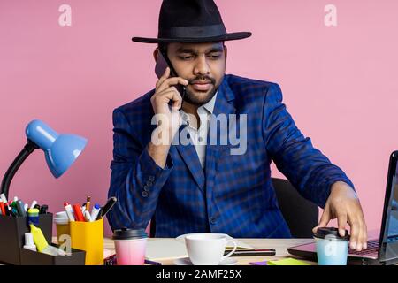 Shot of bearded stylish young businessman in formal wear, having phone conversation with partner, discussing terms of deal, drinking coffee, siiting a Stock Photo