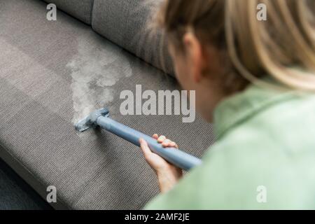 woman cleanig fabric sofa with a steam cleaner at home Stock Photo