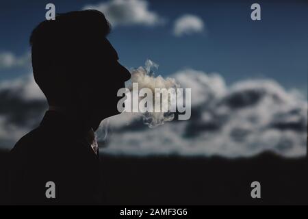 man smokes a cigar and releases smoke. silhouette of smoking man. profile silhouette of a business man who smokes. Stock Photo