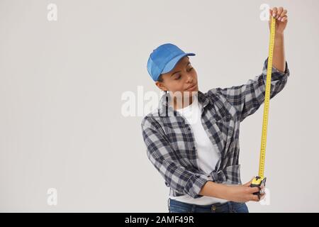 Waist up portrait of pretty female worker holding measuring tape while standing against white background, copy space Stock Photo