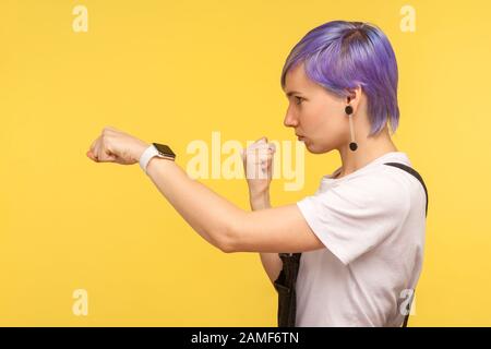 Side view of determined young hipster woman with violet dyed short hair in denim overalls punching with fist, showing boxing gesture, looking confiden Stock Photo