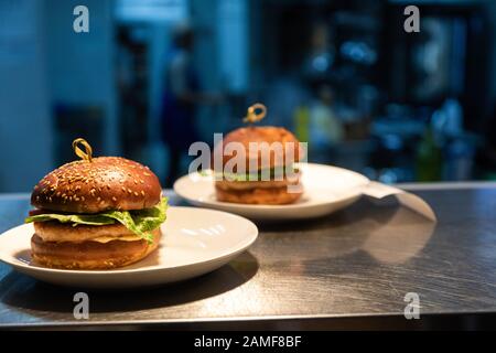 Ready meals hamburgers at the counter for delivery to waiters in a restaurant and kitchen in the background. Stock Photo