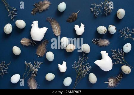 Easter flat lay with eggs, ceramic figurines of chicken and with feathers on blue background. Top view. Stock Photo