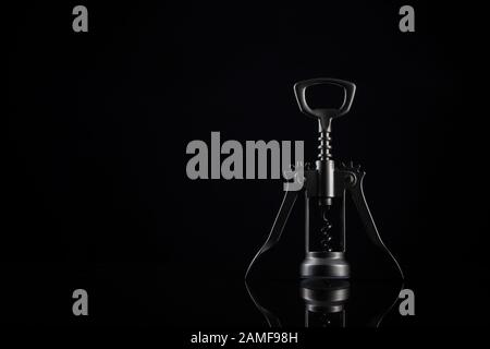 Silver coloured bottle opener on black background. Universal shiny corkscrew tool with spiral for opening beverage drinks isolated on dark backdrop wit Stock Photo
