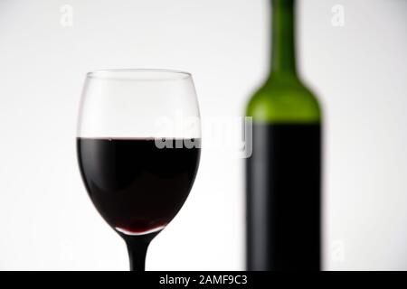 Blurry view of glass of red wine with bottle in the background. Wineglass full of alcohol drink on white background Stock Photo