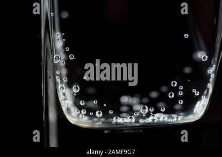 Close up of mineral water bubbles in the glass. Fresh sparkling drink with oxygen balls on dark background Stock Photo