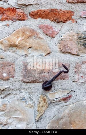 Typical wall made of stones and bricks of ancient Italian house, with rusty iron door hook. Stock Photo