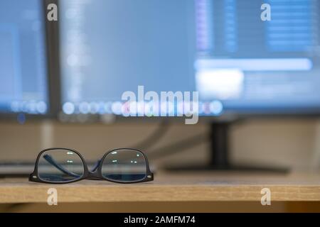 Closeup of protective glasses on an empty desk with blurred computer screen on background. Stock Photo
