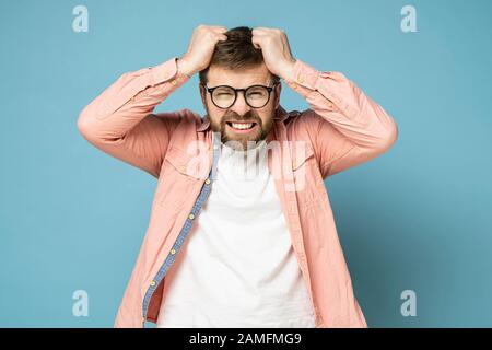 Bearded man in anger and furious, he is trying to tear out his hair on head and grins teeth. Stock Photo