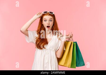 Waist-up portrait impressed, excited and surprised ginger girl, foxy curly hair, take-off sunglasses, seeing amazing discounts in store, hurry up to Stock Photo