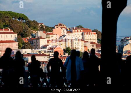 Silhouettes of tourists and visitors admiring the view of Lisbon from St. Peter's observation point (Miradouro de Sao Pedro de Alcantara) in the Bairr Stock Photo