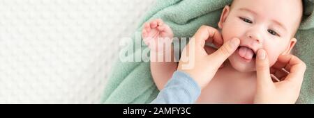Baby face massage banner with copy space. Mother gently stroking baby boy face with both hands. Close up cropped shot. Baby smiling during face massag Stock Photo