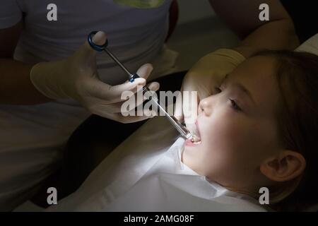 Little girl at dentist office, getting local anesthesia injection into gums, dentist numbing gums for dental work. Pediatric dental care concept. Stock Photo