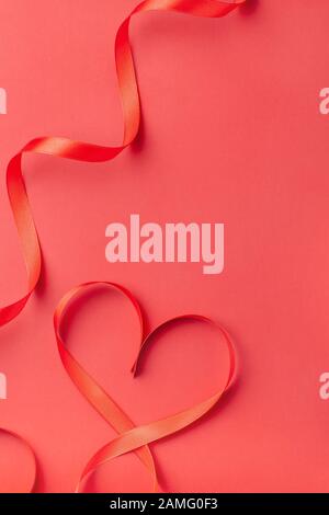 Heart shaped ribbon on red background with copy space. Valentine's Day, Women's Day, Birthday, Mother's Day holiday greeting card concept. Copy space Stock Photo