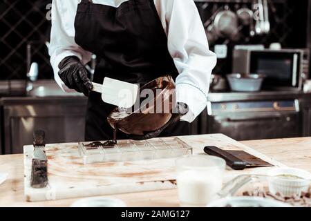 cropped view of chocolatier in apron pouring melted chocolate into ice tray Stock Photo