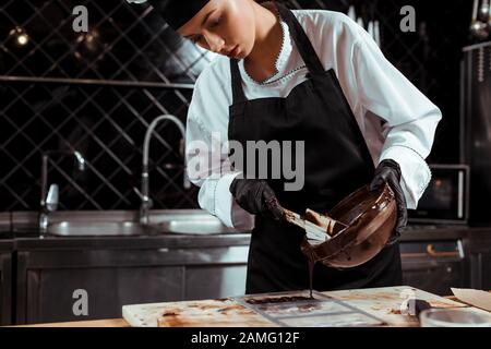 beautiful chocolatier pouring melted chocolate on marble surface Stock Photo