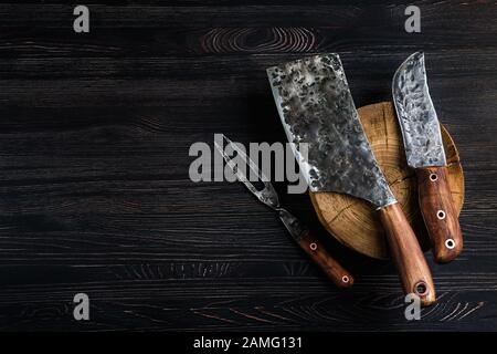 Old butcher meat knife, cleaver and fork on black background Stock Photo